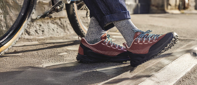 Dettaglio di scarpe KEEN Zionic Collab. Pilgrim Surf Supply indossate in contesto urbano accanto a una bicicletta. Design tecnico e stile outdoor si incontrano in una scarpa comoda, leggera e resistente. Ideale per camminate quotidiane e avventure metropolitane, con suola antiscivolo e tomaia robusta per il massimo comfort e protezione.