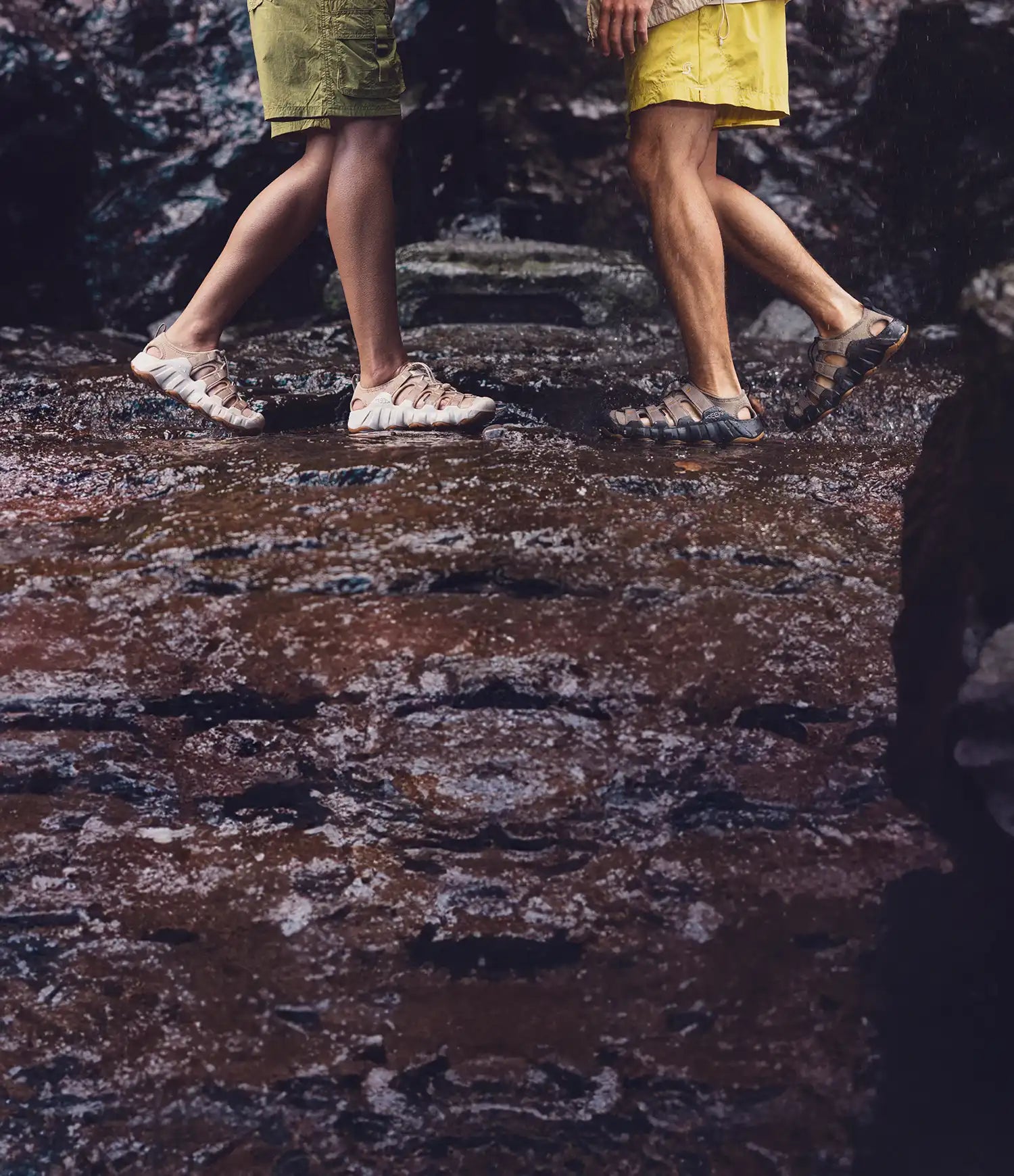Persone che camminano su rocce bagnate vicino a un torrente indossando sandali outdoor KEEN in ambiente naturale.