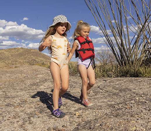 due bambine che corrono sulla roccia e indossano sandali keen newport e seacamp viola e arcobaleno