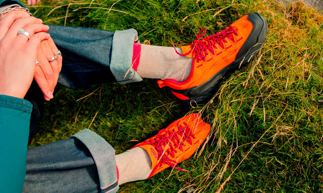 Dettaglio di persona seduta sull’erba che indossa scarpe KEEN Jasper Zionic orange black.
