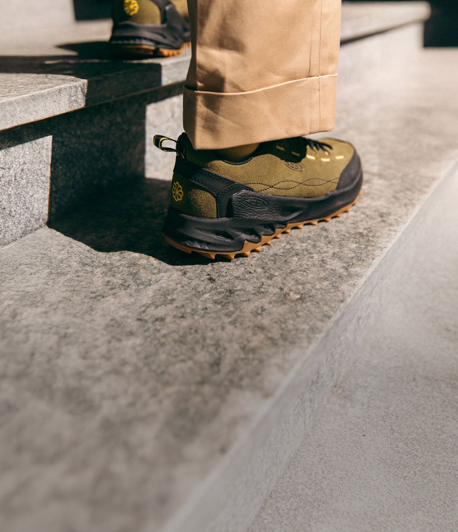 Scarpa KEEN Jasper Zionic in tonalità verde oliva indossata su gradini in pietra, in un contesto lifestyle cittadino.