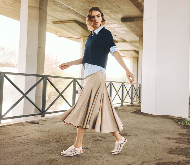 Donna in piedi sull’erba vicino a un ponte, indossa sandali Keen Hyperport H2 da donna in colore rosa, in un contesto naturale e rilassato.