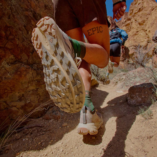 Runner con scarpe KEEN da trail running su un sentiero roccioso, con suola in primo piano.