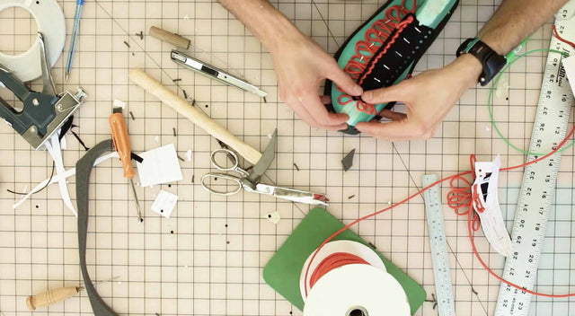 Mani di artigiano al lavoro su un prototipo di scarpa KEEN, circondato da strumenti e materiali di design