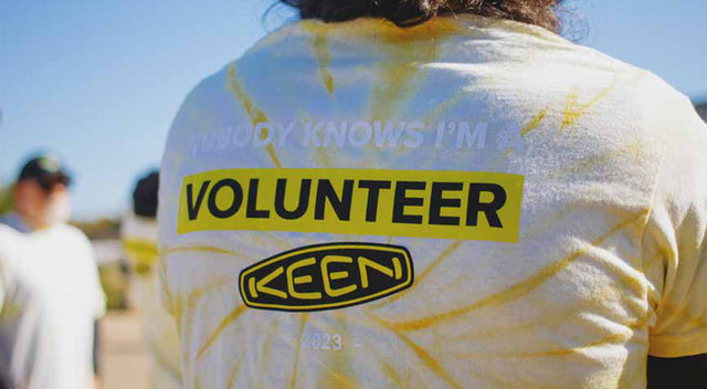 Maglietta con la scritta Volunteer e logo KEEN, simbolo delle attività di volontariato supportate dall’azienda.