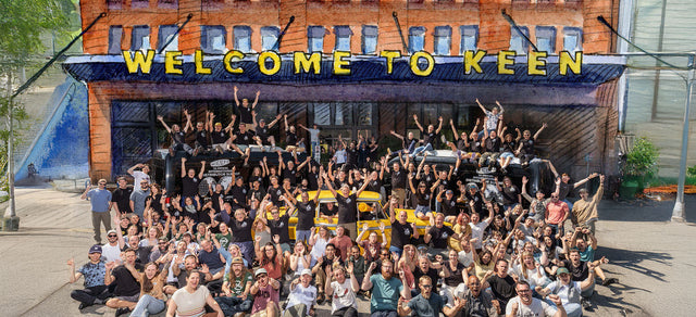 Grande gruppo di persone sorridenti davanti alla sede KEEN con la scritta Welcome to KEEN, simbolo di comunità e collaborazione