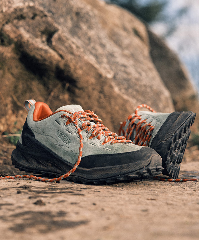 Scarpa KEEN Jasper Zionic uomo verde con lacci arancioni, posata su terreno roccioso outdoor per attività trekking